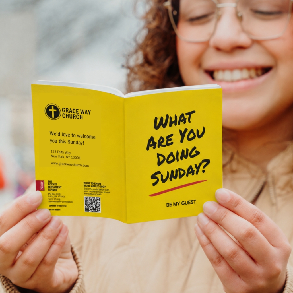 A smiling person holds a yellow pamphlet that reads, “What are you doing Sunday? Be my guest,” with Grace Way Church’s logo, address, website, and a QR code on the cover.