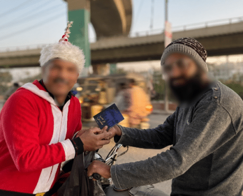 A person dressed as Santa Claus hands a small dark-colored book to a person sitting on a motorcycle.